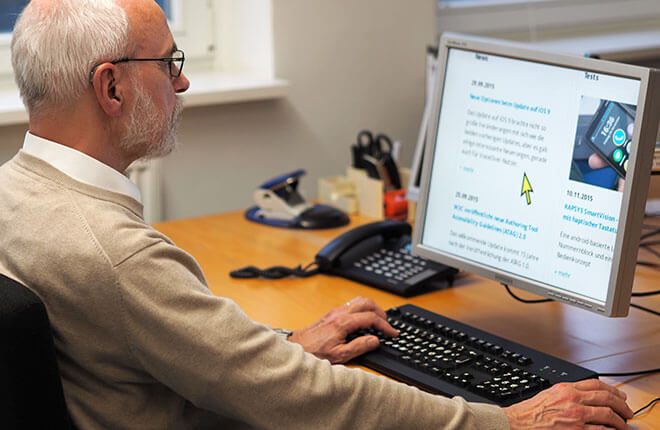 Älterer Mann sitzt vor einem Monitor, der Inhalt des Bildschirms ist vergrößert.